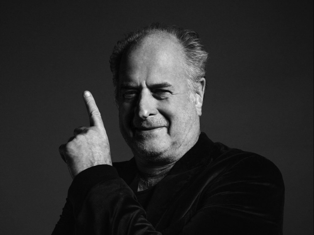 Black and white photo of Michael Gudinski pointing his finger above his head