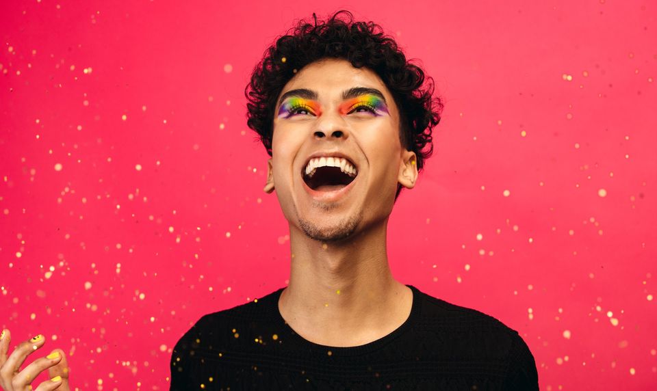 portrait of person laughing with glitter and makeup on pink background