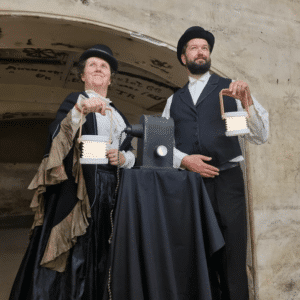 Two performers in Victorian costumes holding lanterns outdoors
