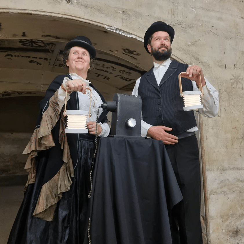 Two performers in Victorian costumes holding lanterns outdoors
