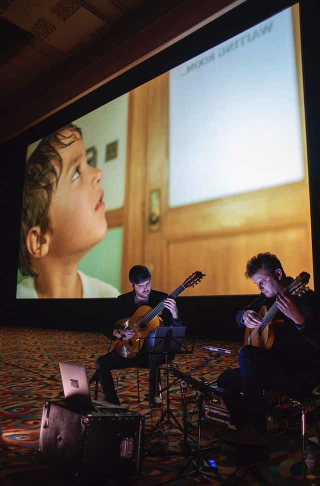 Two guitarists performing beneath large projected image screen