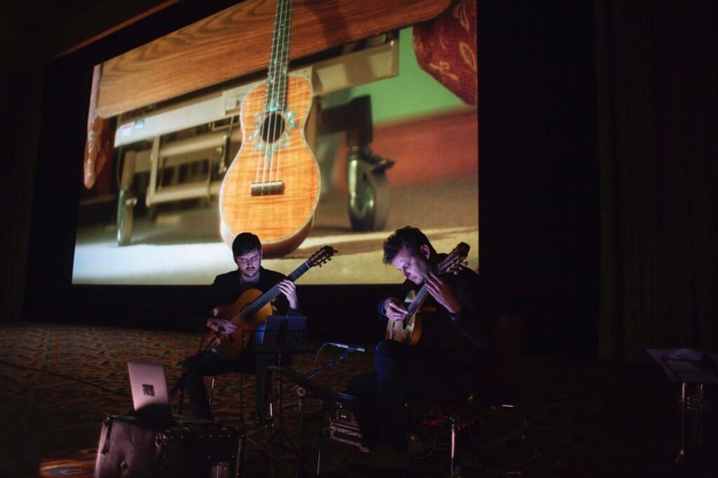 Two guitarists performing with projected ukulele image backdrop