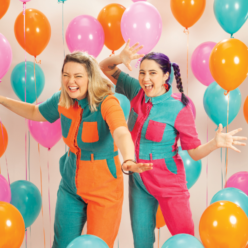 Two women in colourful matching jumpsuits surrounded by balloons