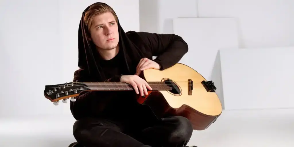 Young musician in black hoodie sitting with acoustic guitar
