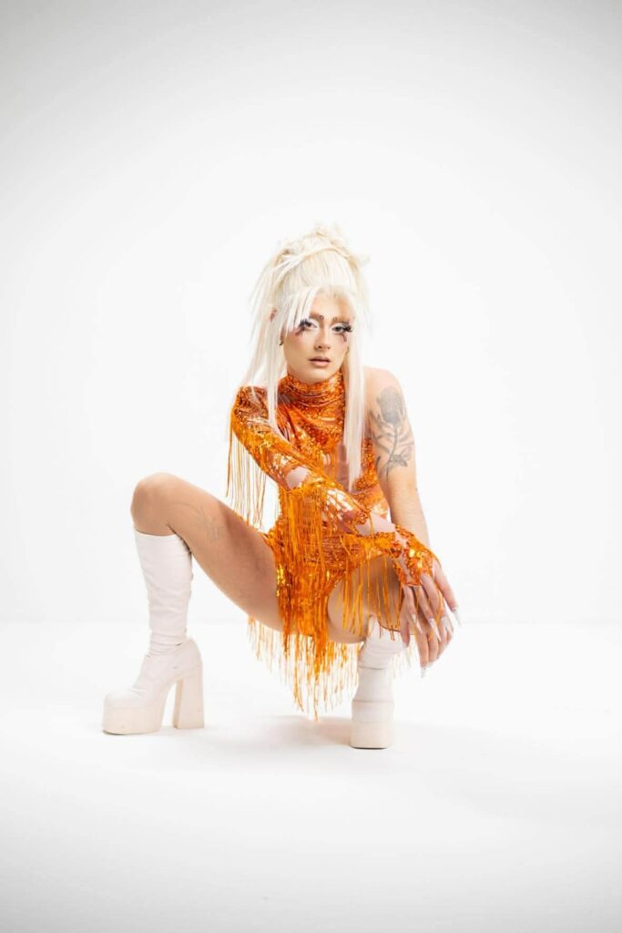 Performer in orange sequin fringe costume and white platform boots