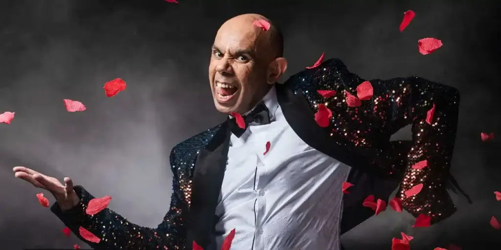Bald performer in sequin tuxedo surrounded by red rose petals