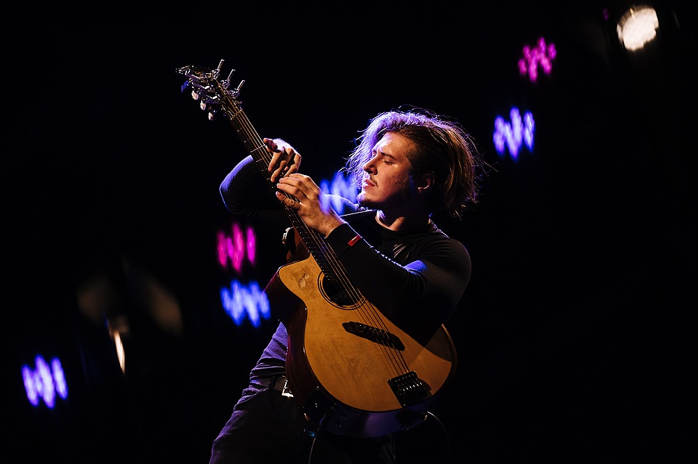 Young male guitarist performing on stage with acoustic guitar