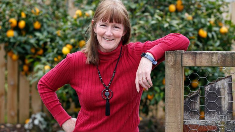 Woman in red jumper smiling by wooden garden fence