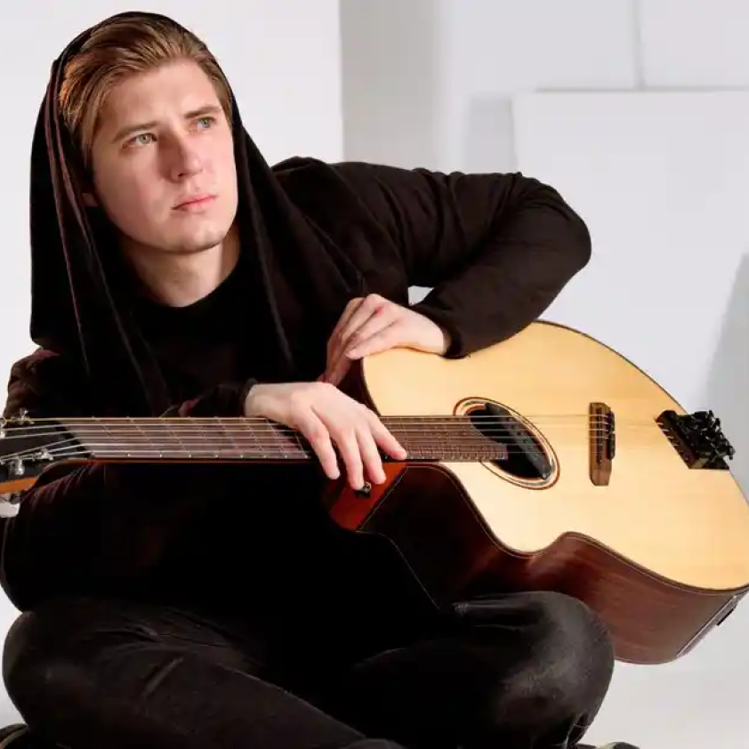 Young male guitarist in black hoodie holding acoustic guitar