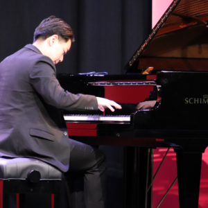 Young male pianist performing on Schimmel grand piano on stage