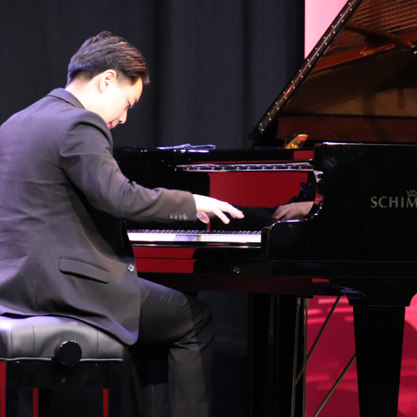 Young male pianist performing on Schimmel grand piano on stage