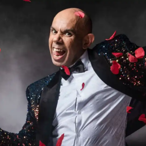Bald performer in sequin tuxedo surrounded by rose petals