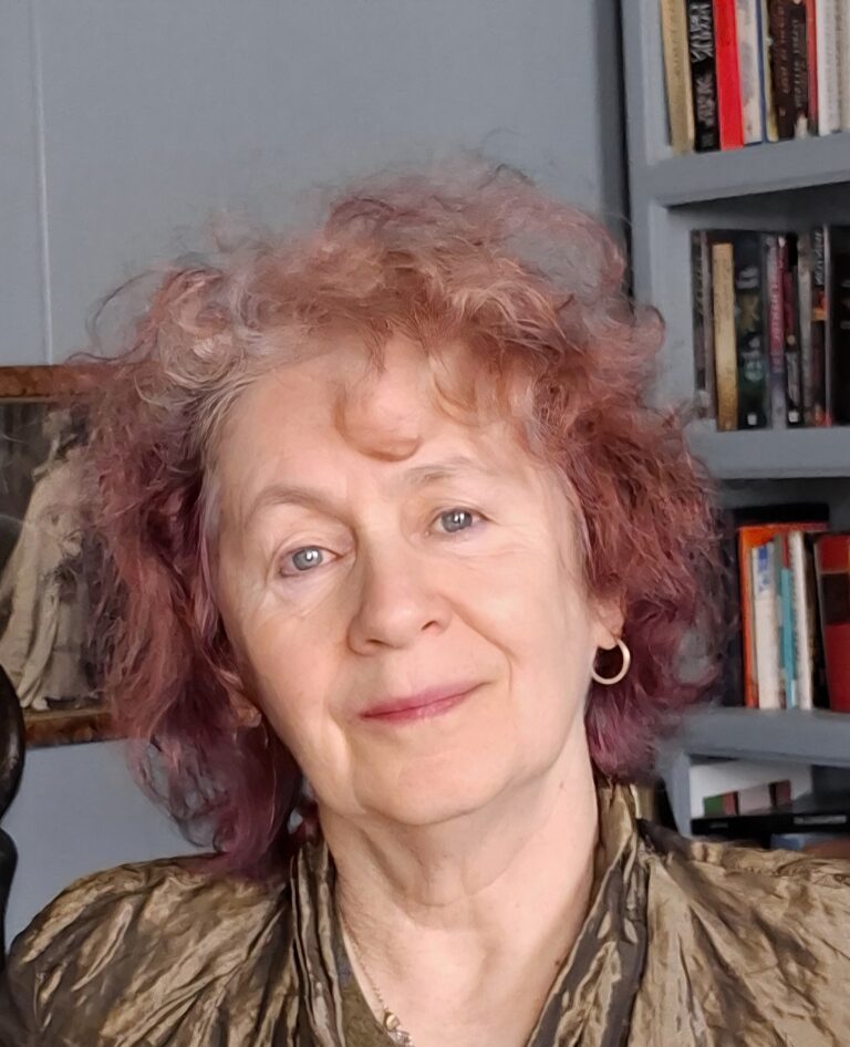Older woman with curly pink hair smiling before bookshelves