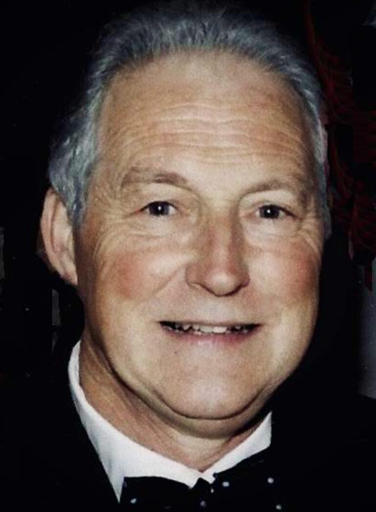 Older man with grey hair smiling in formal attire
