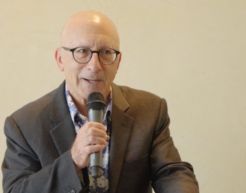 Elderly man with glasses speaking into a microphone