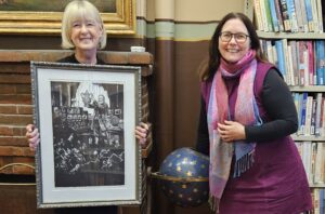 Two women smiling holding framed artwork in a library