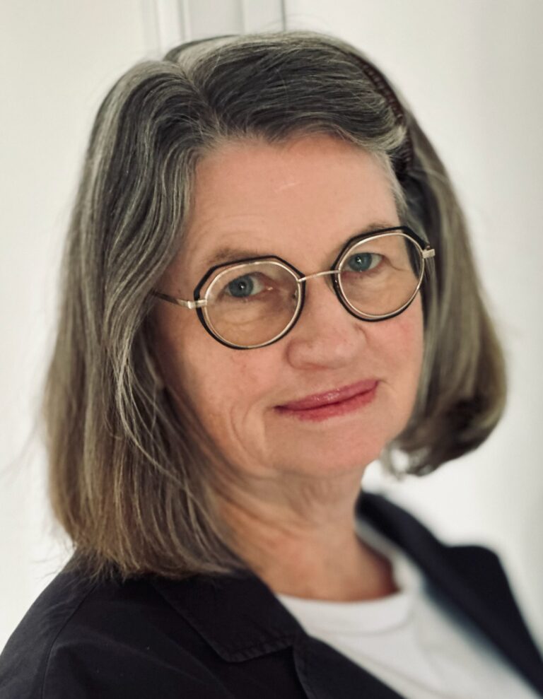 Mature woman with grey hair and round glasses smiling