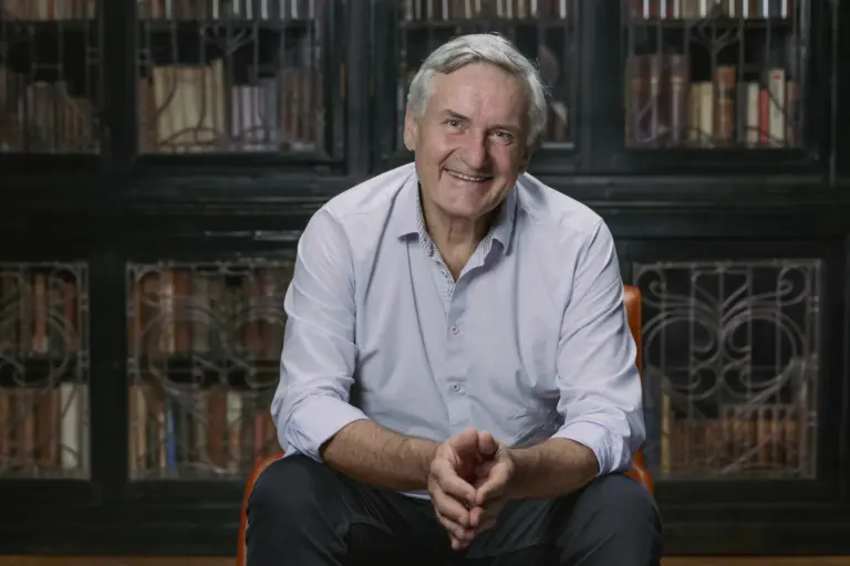 Smiling older man seated in front of ornate bookcase