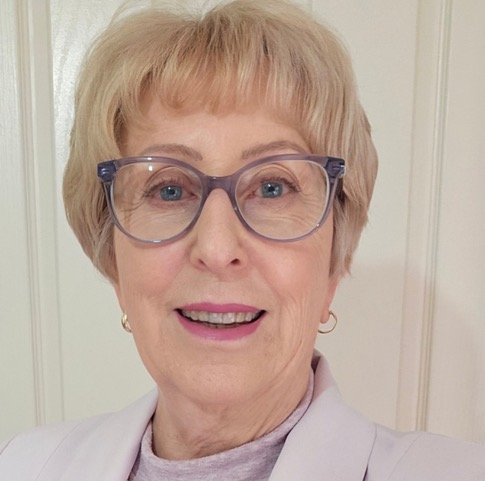 Smiling older woman with short blonde hair and grey glasses