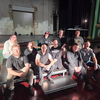 Group of nine people posing together inside a theatre