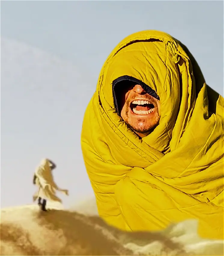 Man laughing wrapped in yellow sleeping bag in desert