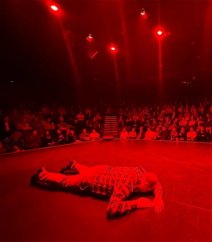Performer lying on stage in dramatic red lighting