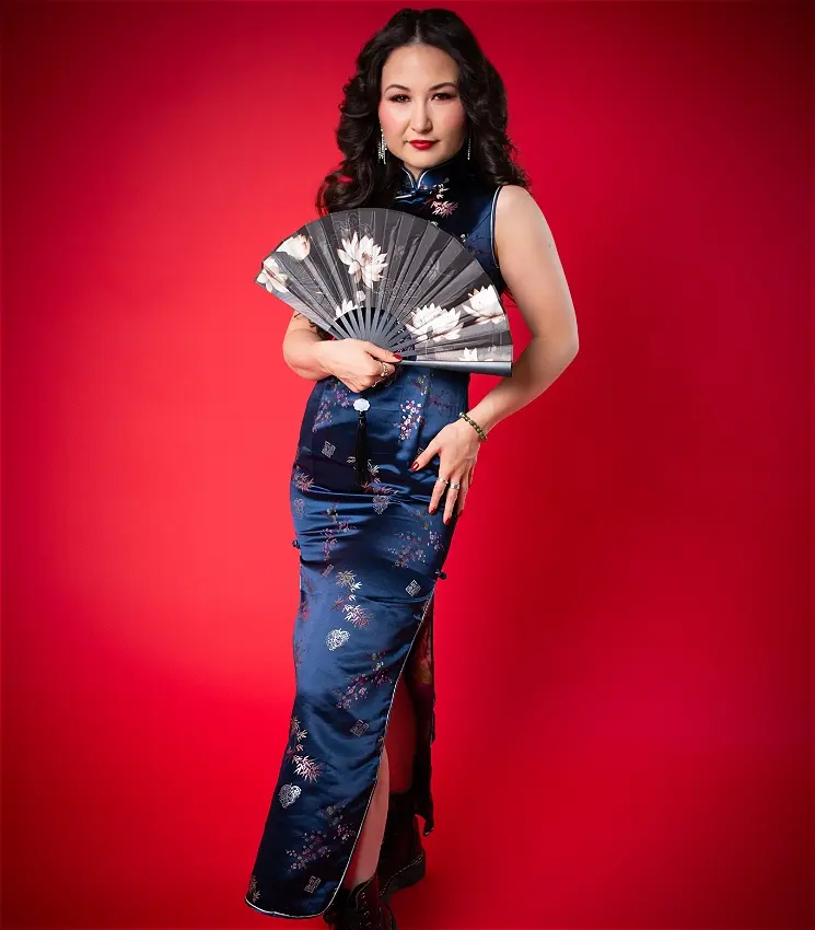 Woman in blue qipao holding decorative fan against red background
