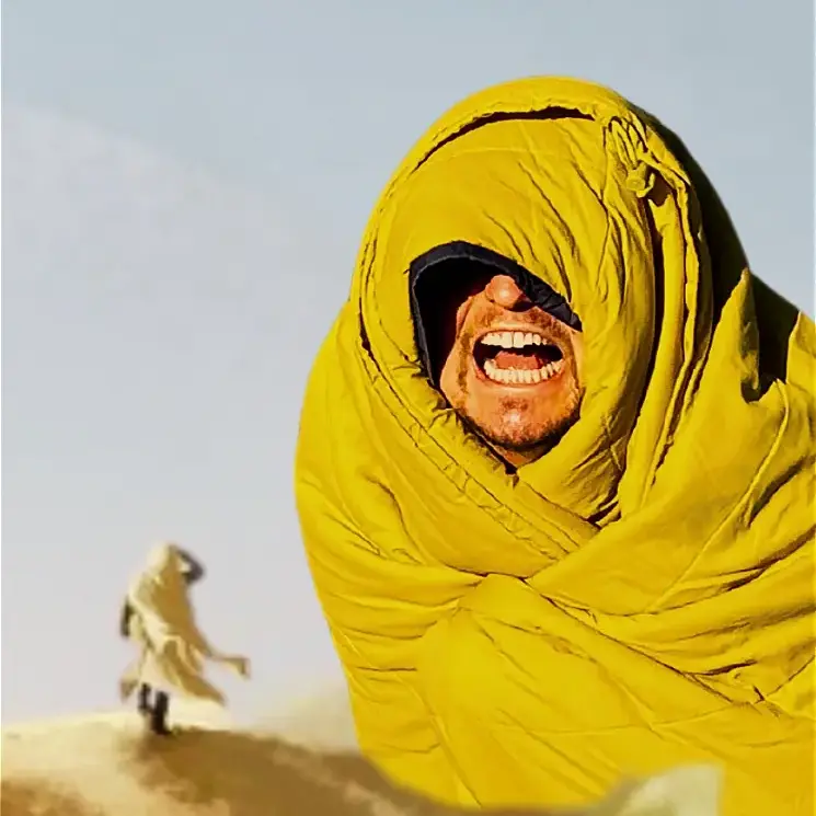 Laughing man wrapped in yellow sleeping bag in desert