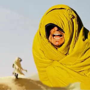 Laughing man wrapped in yellow sleeping bag in desert